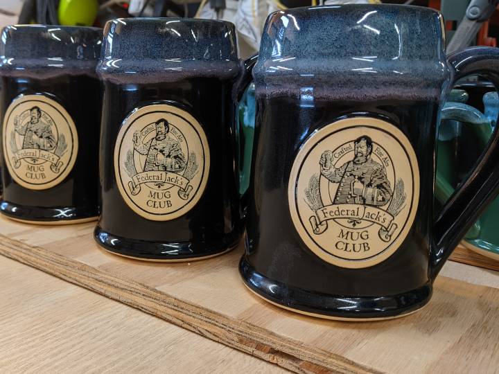 Purple and blue beer steins with image of a man holding a beer and the text "Crafted Fine Ales. Federal Jack's Mug Club".