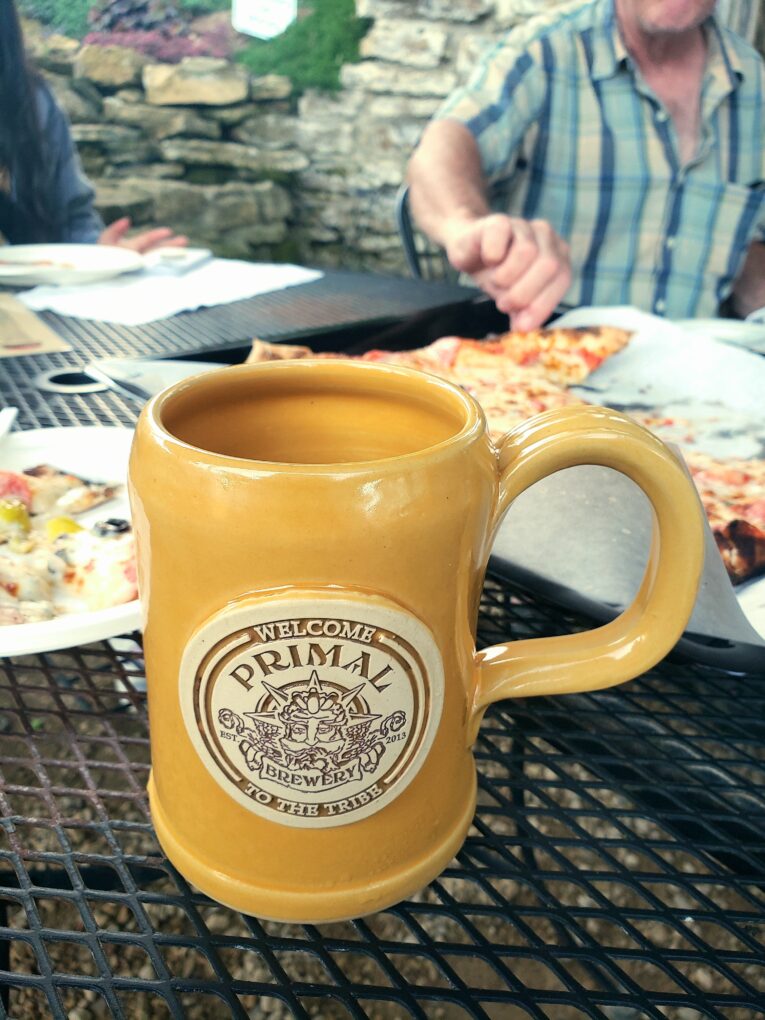 yellow ceramic beer stein with logo for a brewery, people eating pizza in the background