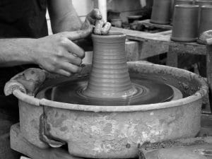 Two hands shaping a clay mug on a potter's wheel.