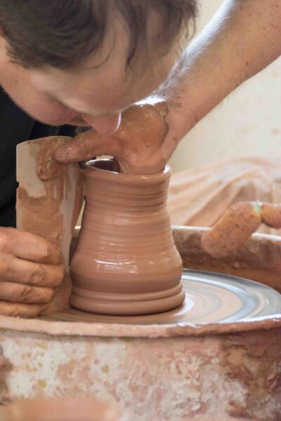 Close up image of a person using his hands to shape a clay mug on a pottery's wheel.