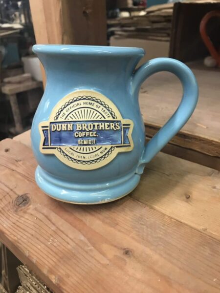Blue coffee mug with a clay logo medallion that has the text "Dunn Brothers Coffee".
