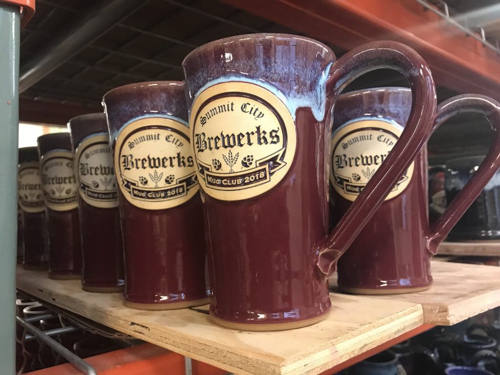 Tall red beer stein with handle and a clay logo medallion reading "summit city brewworks".