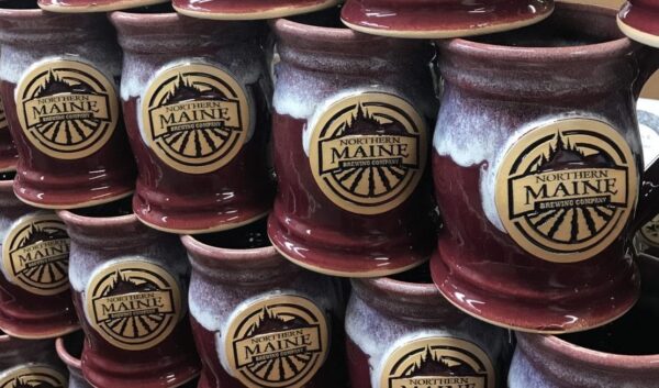 Large group of red beer steins stacked with clay logo medallion with the text "Northern Maine Brewing Company".