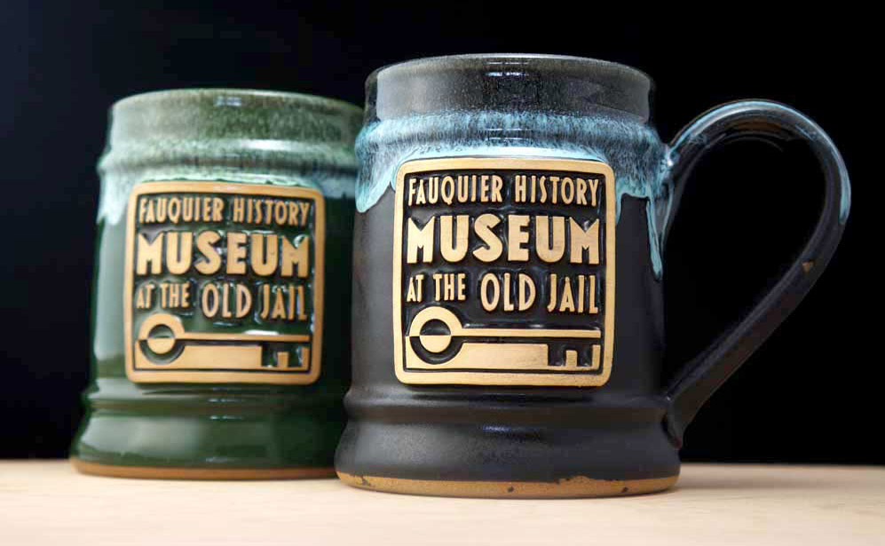 A dark green and black coffee mug with a museum logo. 