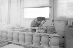 man hand throwing a clay pot on a pottery wheel with clay beer steins in the foreground.