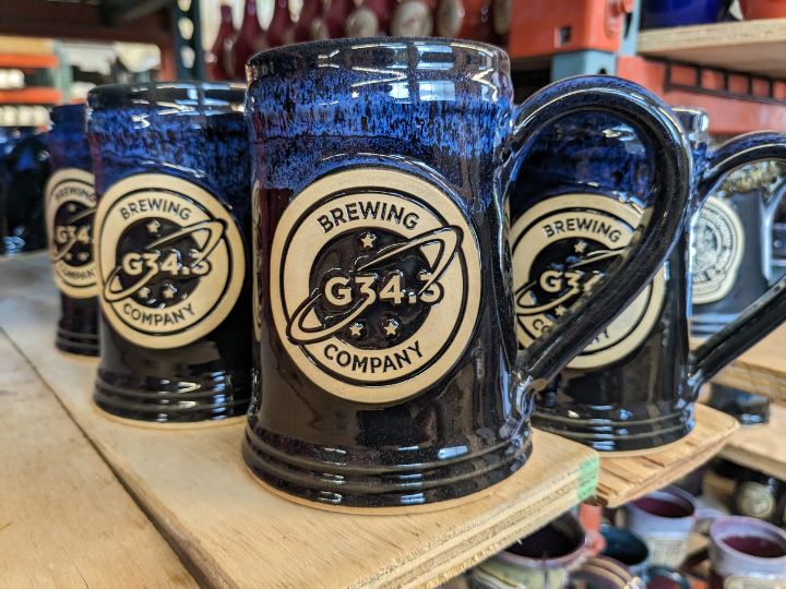 Black and blu beer steins on a wood plank with a custom logo medallion reading "g34.3 brewing company".