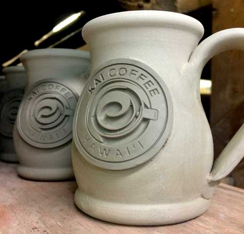 Clay coffee mug with Text "Kai Coffee Hawai'i" with an overhead view of an illustration of a coffee mug.