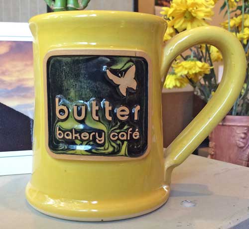 Yellow coffee mug with a logo medallion with the text "butter bakery cafe" with an illustration of a butterfly.