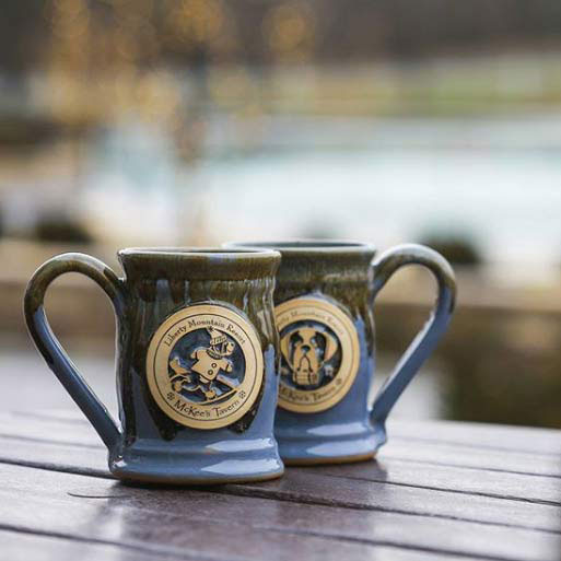 two blue and brown clay mugs on a picnic table with blurred background.