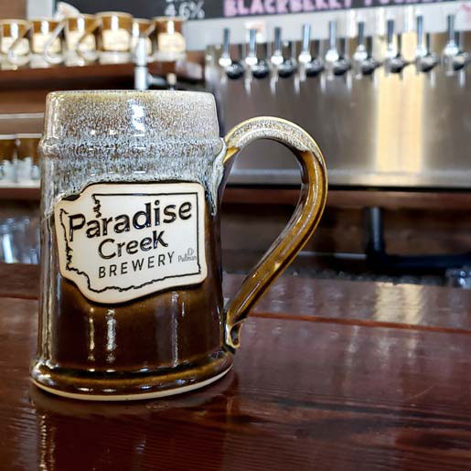 brown and white beer stein on a bar counter with a logo that reads 'paradise creek brewery'.