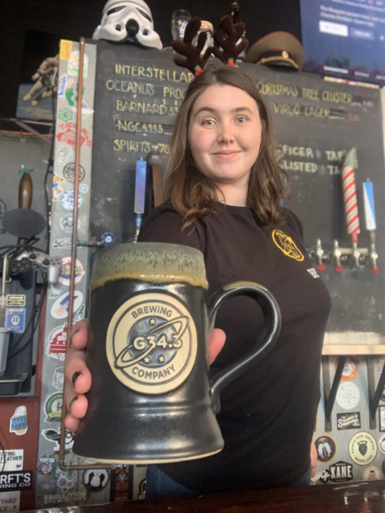Woman holding black beer stein featuring a space themed logo.