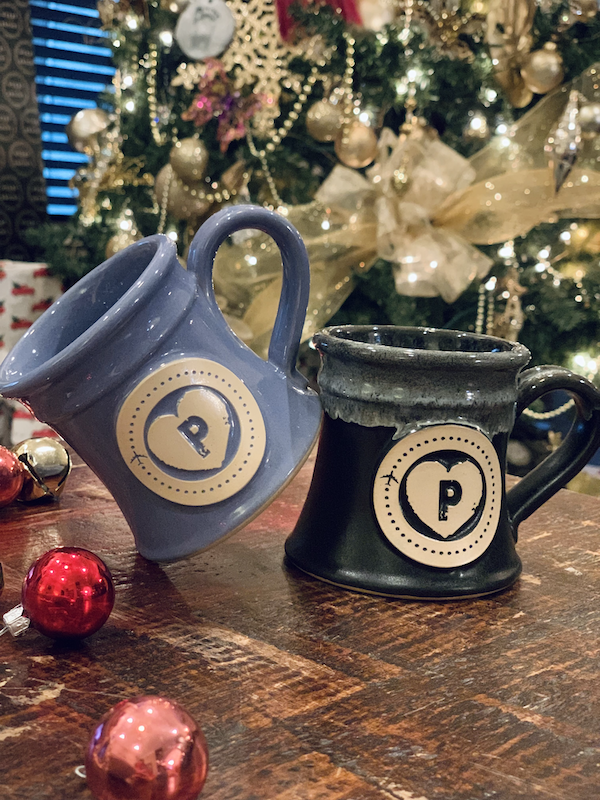 Purple and black coffee mugs sitting on a table with a christmas tree in the background.