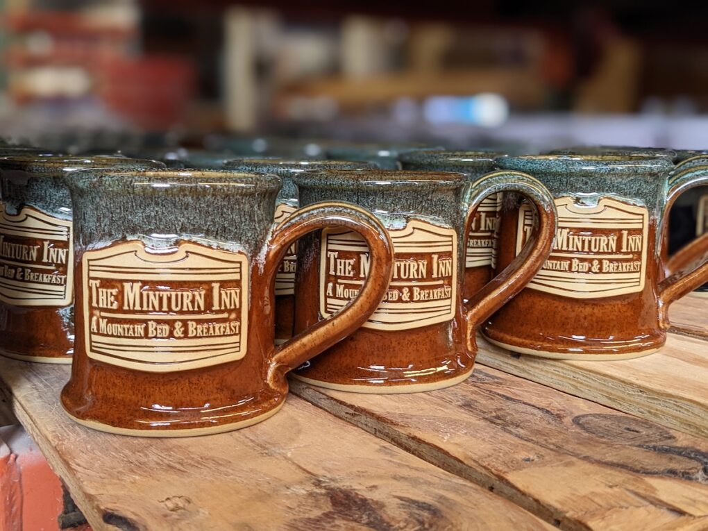 Branded handmade coffee mugs on a wood platform.