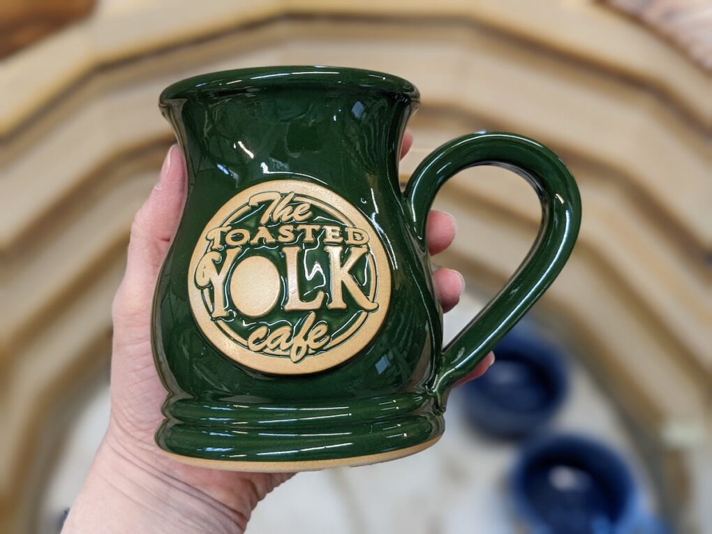 Handmade mug held in a hand with egg logo.