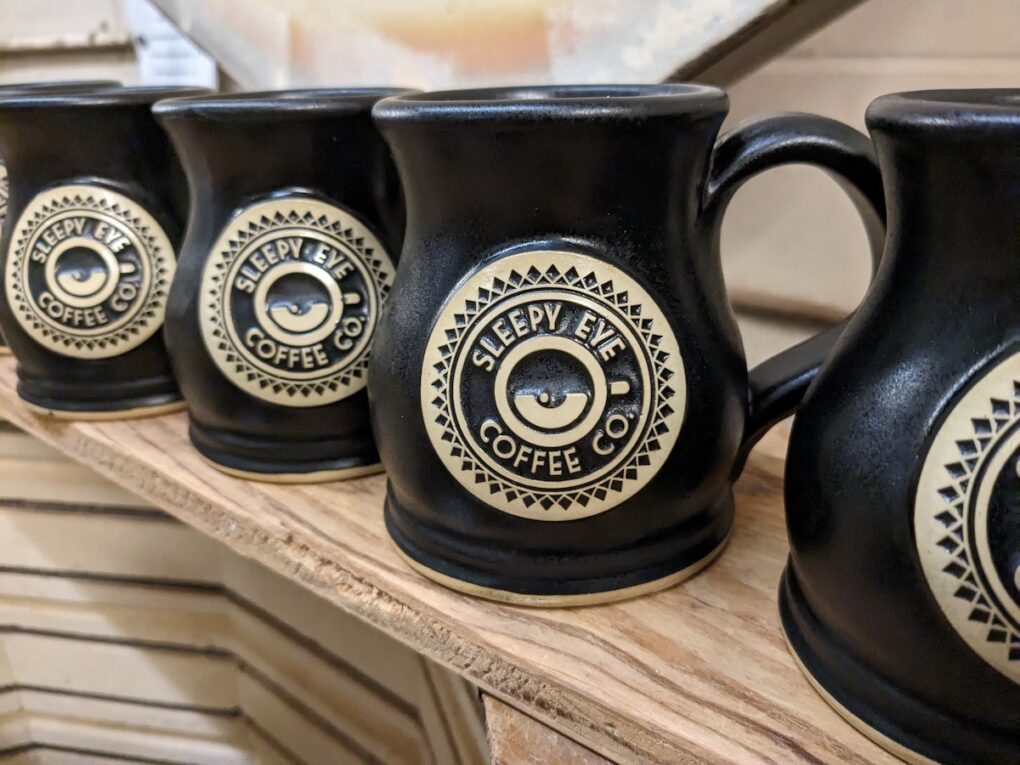 Four black coffee mugs with logo of coffee shop.