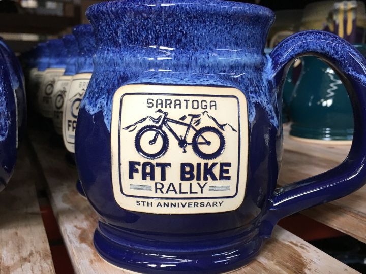 Blue beer mug with a clay medallion that features an illustration of a bicycle and the text "Saratoga fat bike rally. 5th Anniversary". 