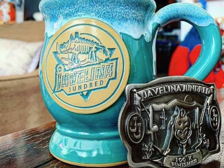 Green coffee mug with a logo medallion and a face finisher buckle with the words "Javelina Jundred".