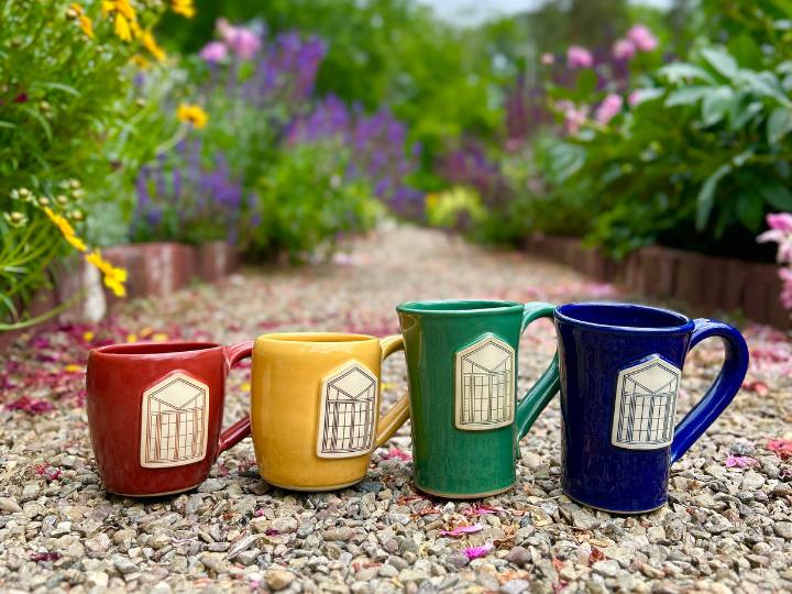 Group of four brightly colored coffee mugs sitting on a gravel path in a garden.