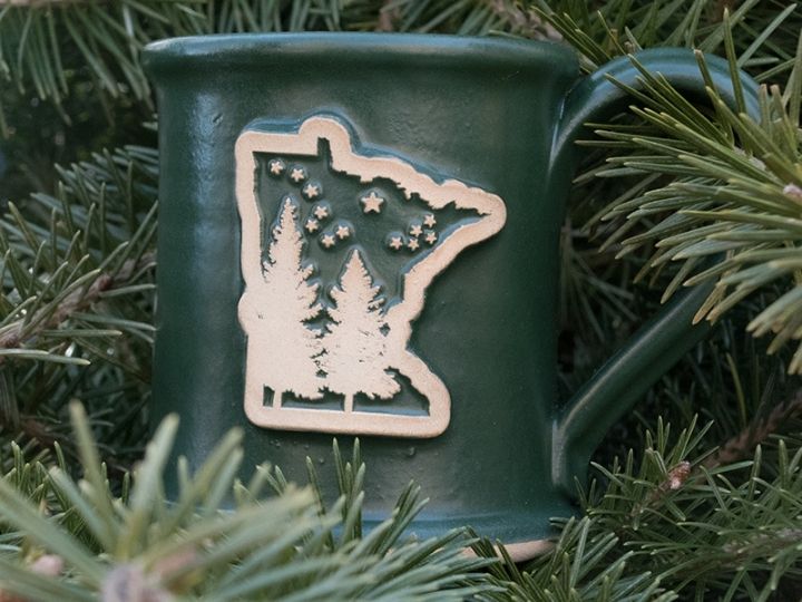 green coffee mug with outline of the state of minnesota surrounded by greenery