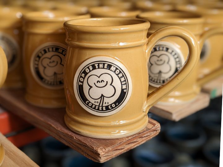 Row of yellow coffee mugs with a logo of a shamrock