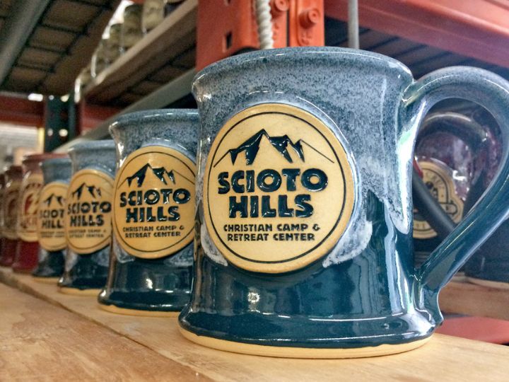 row of green coffee mugs with 'scioto hills' camp logo on them