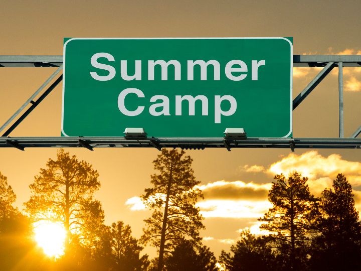 green road sign that reads 'summer camp' with pine trees in the background