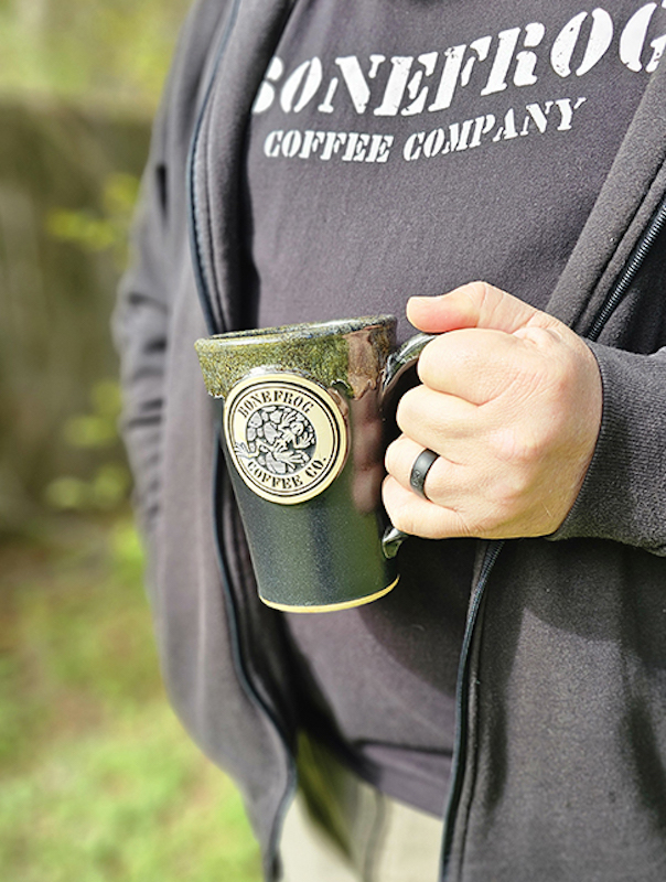 image showing a person holding a green coffee mugs with an image of a frog on it and the text 'bonefrog coffee'