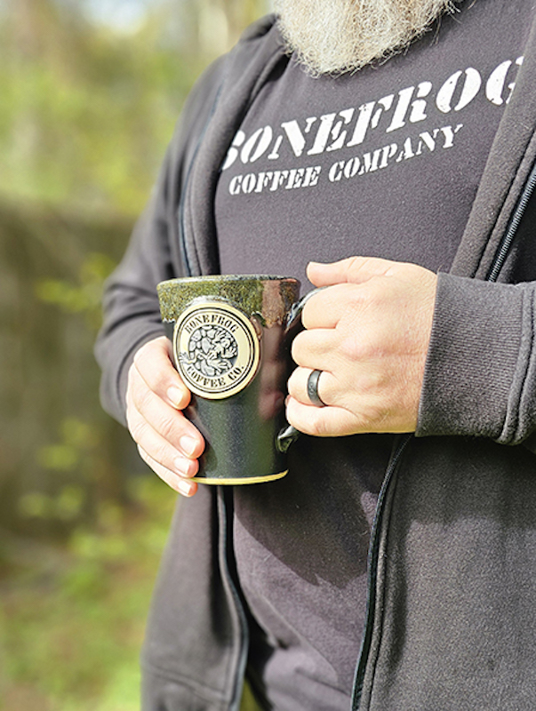 image showing a person holding a green coffee mugs with an image of a frog on it and the text 'bonefrog coffee'