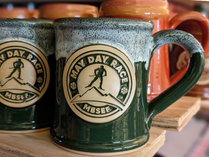 green coffee mugs with a logo of a figure skiing in a may day race