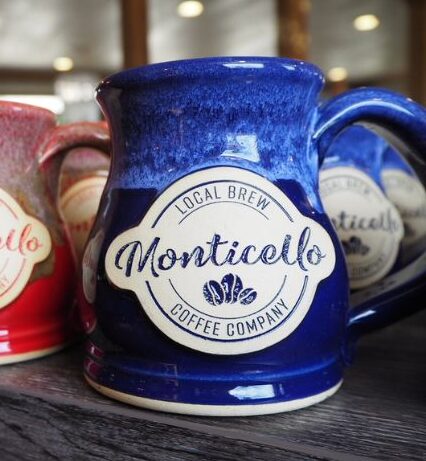 two red and one blue coffee mug on a wood table with a logo for 'monticello coffee company' on them