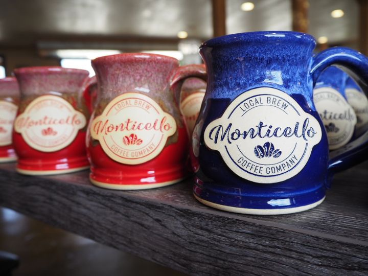 two red and one blue coffee mug on a wood table with a logo for 'monticello coffee company' on them