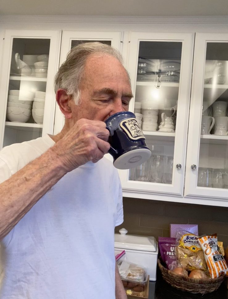 hand holding a black coffee mug with blue glazed rim. the coffee mug has a round clay medallion logo of a pirate tattoo shop