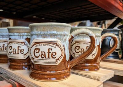 brown and white coffees mugs on a shelf with the logo for 'abita springs cafe'