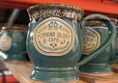 green and brown coffee mugs on a shelf with the logo for 'morning glory cafe'