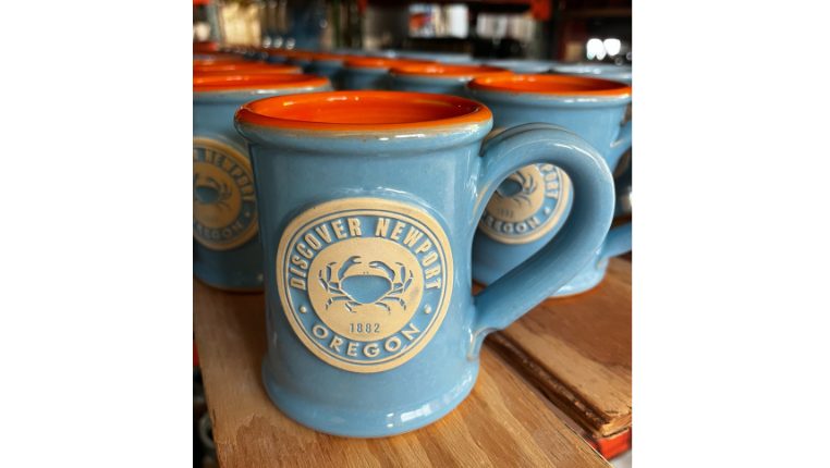 blue and orange mug with brand logo sitting on a wood plank