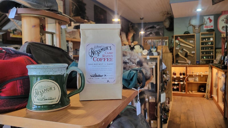 green coffee mug sitting on a retail shelf in a sporting goods store next to a bag of coffee beans