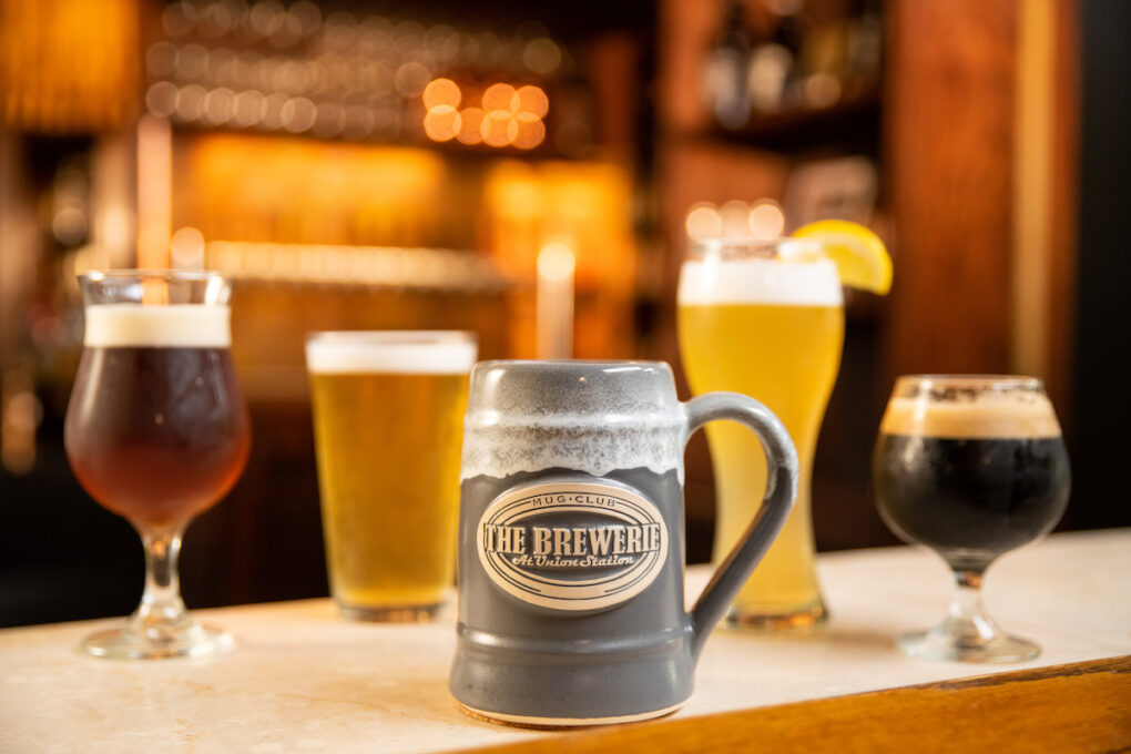 grey stoneware logo beer stein on a bar in front of glasses of beer