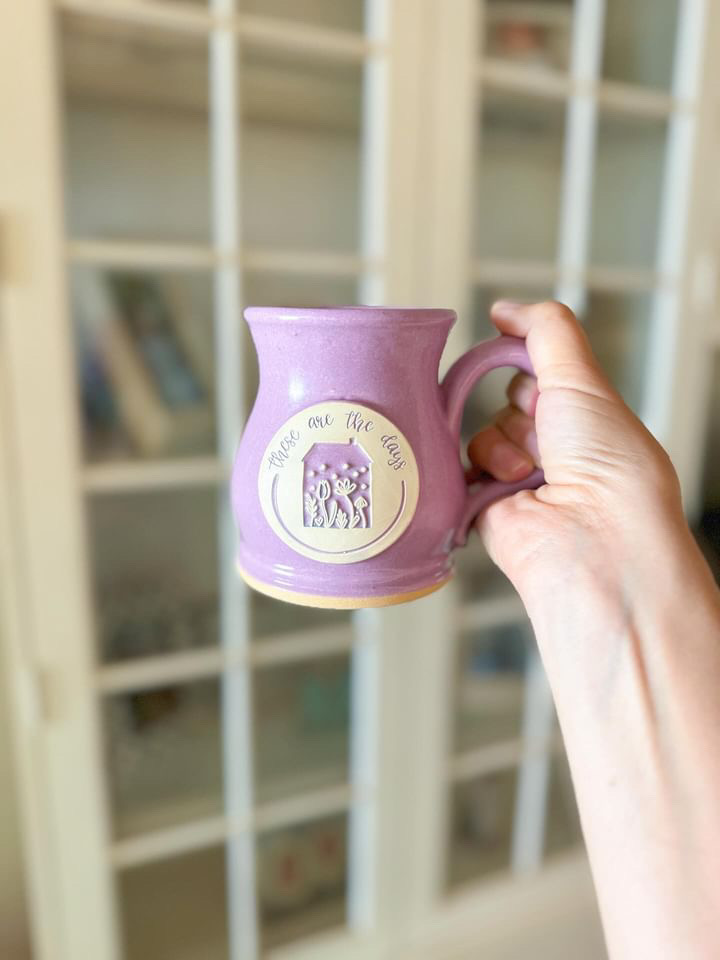 outstretched hand holding a purple coffee mug with a logo on it