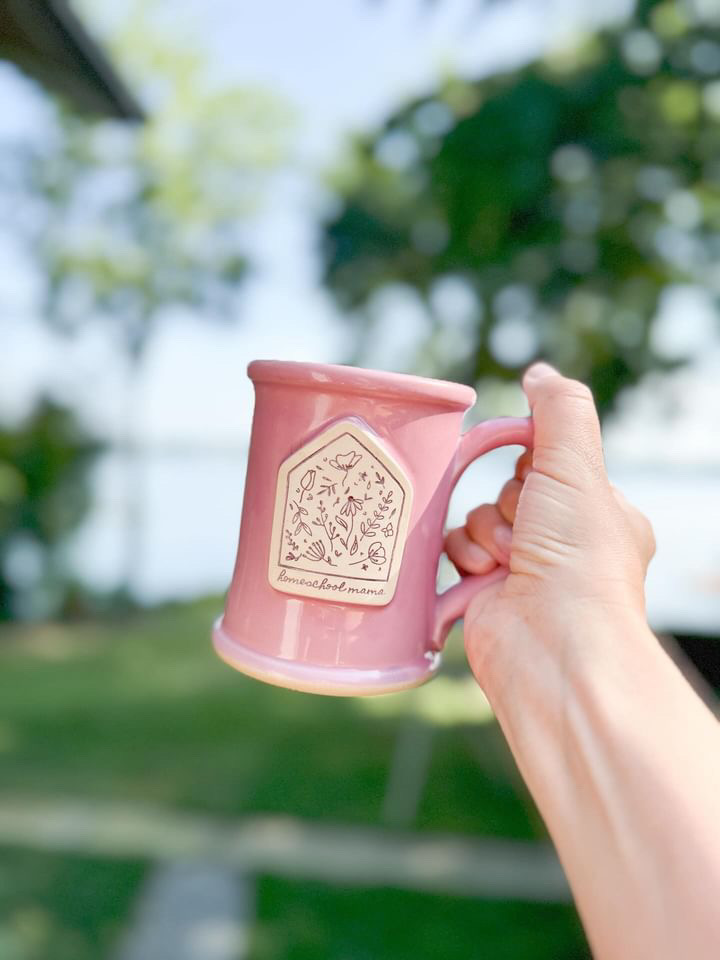 outstretched hand holding a pink coffee mug with a logo on it