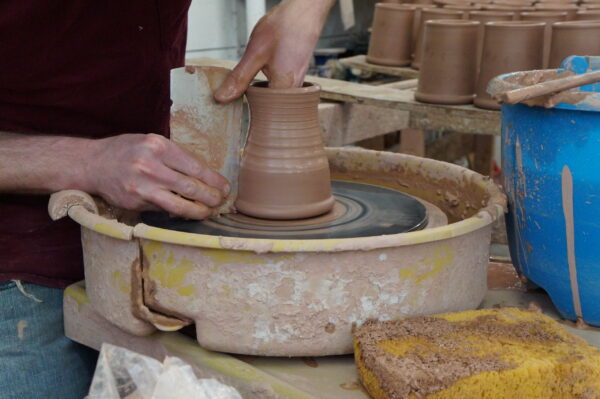 image of a person's hands making a mug out of clay on a pottery wheel