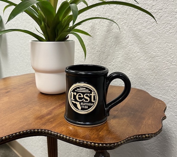 black coffee mug on a wood table, with a plant in the background