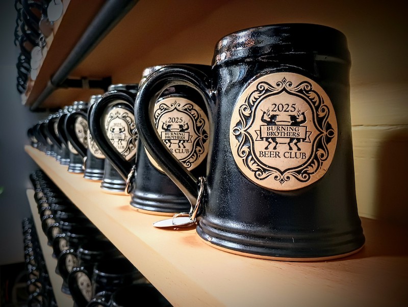 black beer steins on wooden shelves with a brewery logo