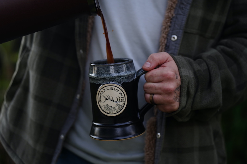 person holding a tall coffee mug while they pour coffee